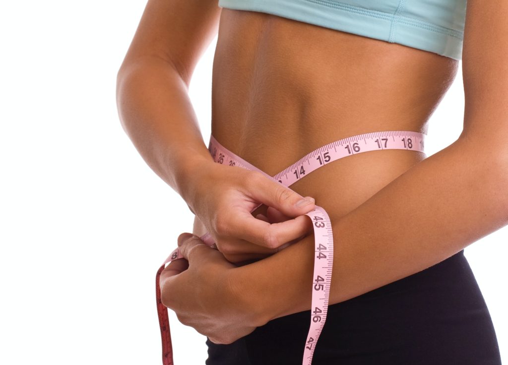 fit lady with her holding a measuring tap around her stomach